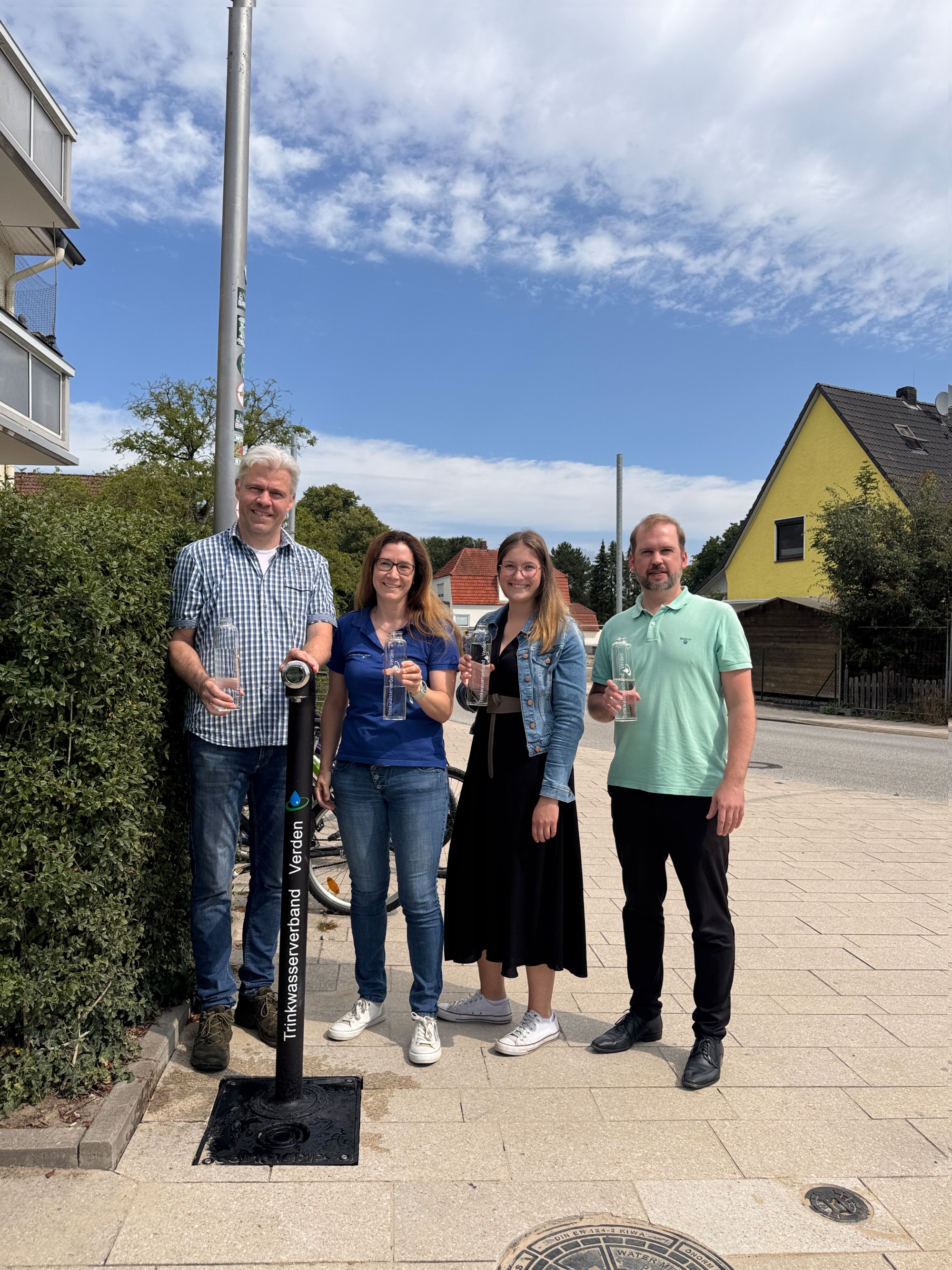 Trinkwasserzapfsäule Oyten.jpg Marco Schaubitzer (r.), Celina Weide (2. v. r.) und Michael Bruns (l.) aus der Oytener Gemeindeverwaltung gehörten zusammen mit Anne Hinrichs vom Trinkwasserverband Verden zu den ersten Nutzern der neuen Trinkwasserzapfsäule. Alle Vier stehen um die neue Trinkwasserzapfsäule herum.